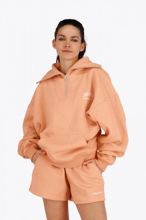 Osaka Women Half Zip Sweater | Peach Osaka women half zip sweater in peach with white logo. Front flatlay view