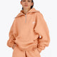 Woman wearing the Osaka women half zip sweater in peach with white logo. Front view