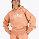 Woman wearing the Osaka women hoodie in peach with white logo. Front view