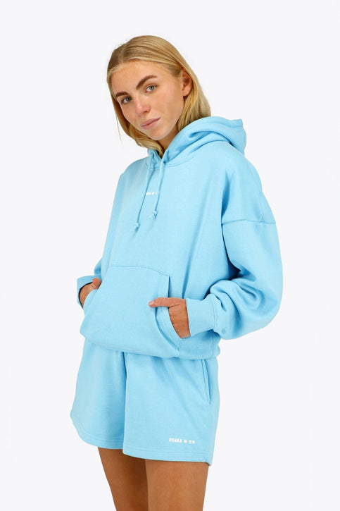 Osaka Women Hoodie | Blue Topaz Osaka women hoodie in light blue with white logo. Front flatlay view