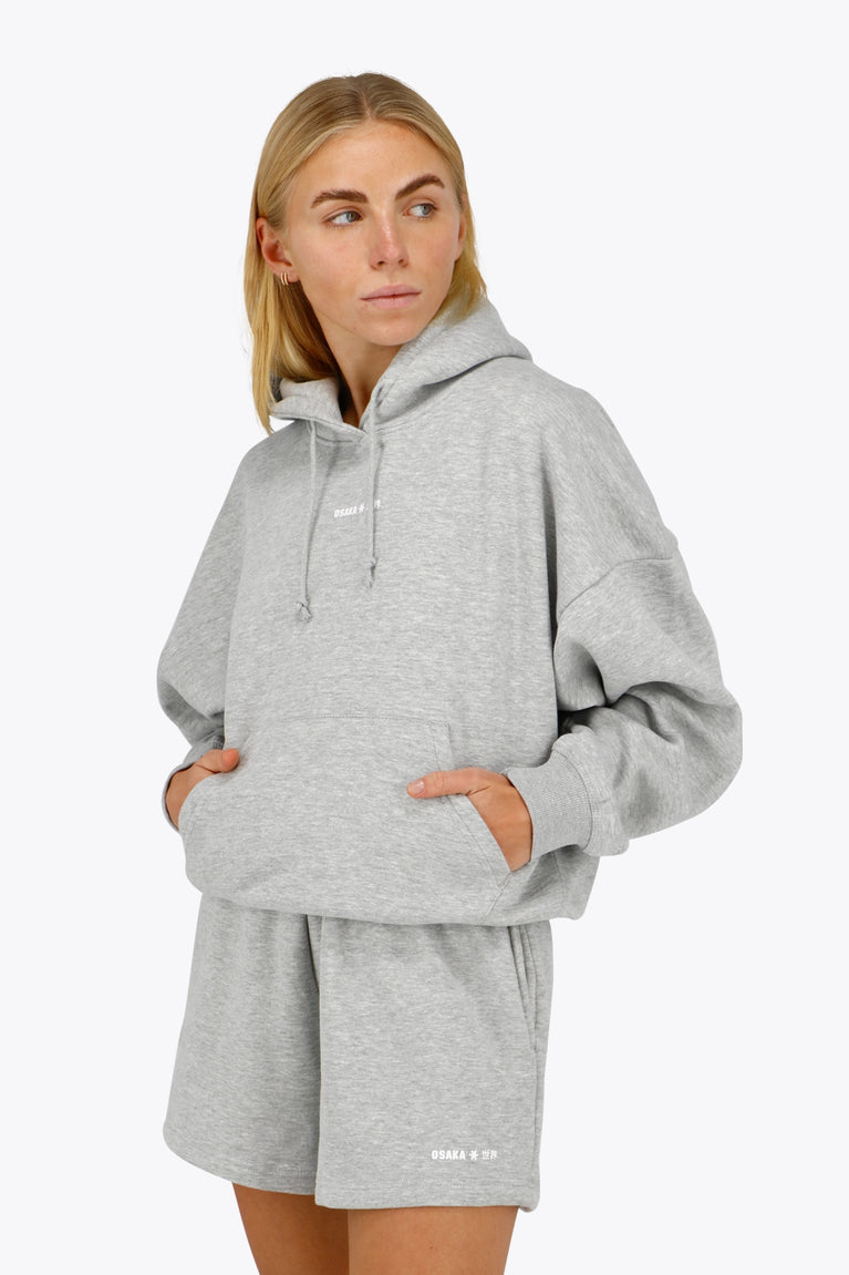 Woman wearing the Osaka women hoodie in heather grey with white logo. Front view