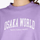 Woman wearing the Osaka women sweater in light purple with logo in white. Front detail logo view