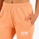 Woman wearing the Osaka women sweatpants in peach with logo in white. Front detail logo view