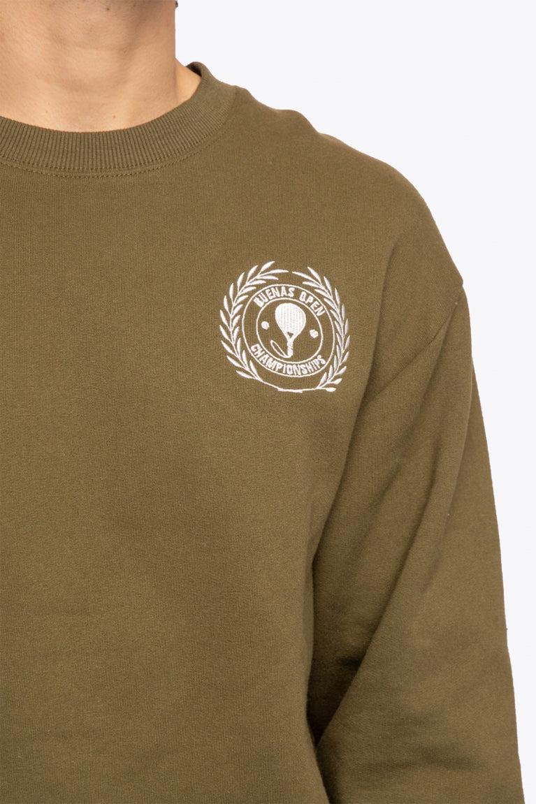 Man wearing the Osaka x Buenas Open sweater in army green. Front detail logo view