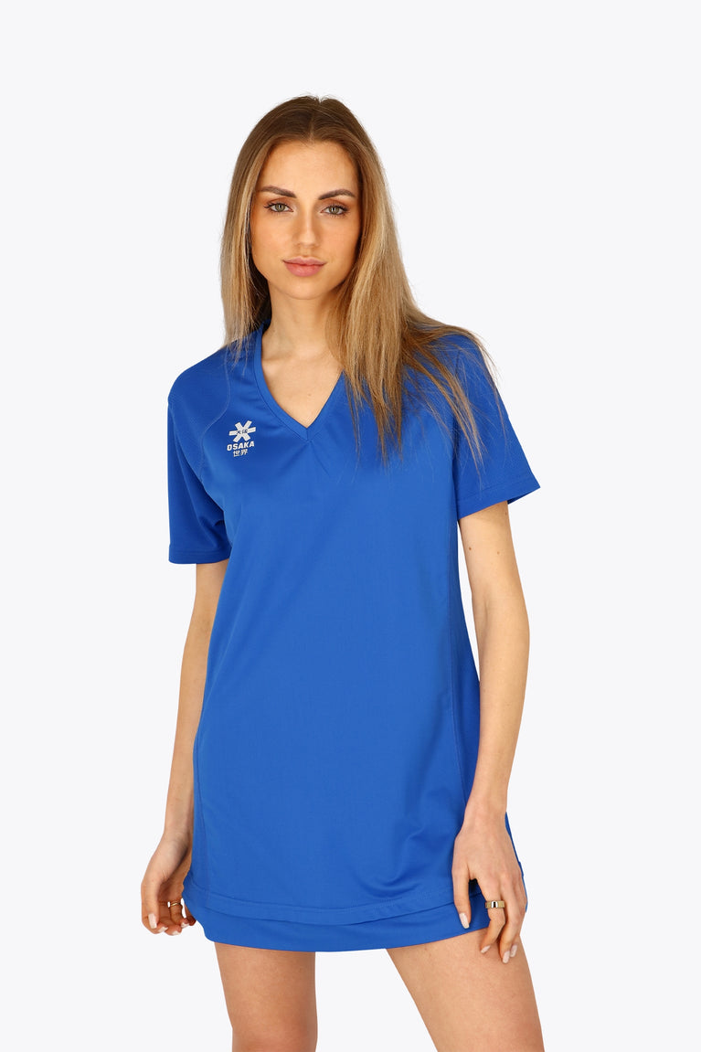 Woman wearing the Osaka women v-neck tech dress in princess blue with logo in grey. Front view