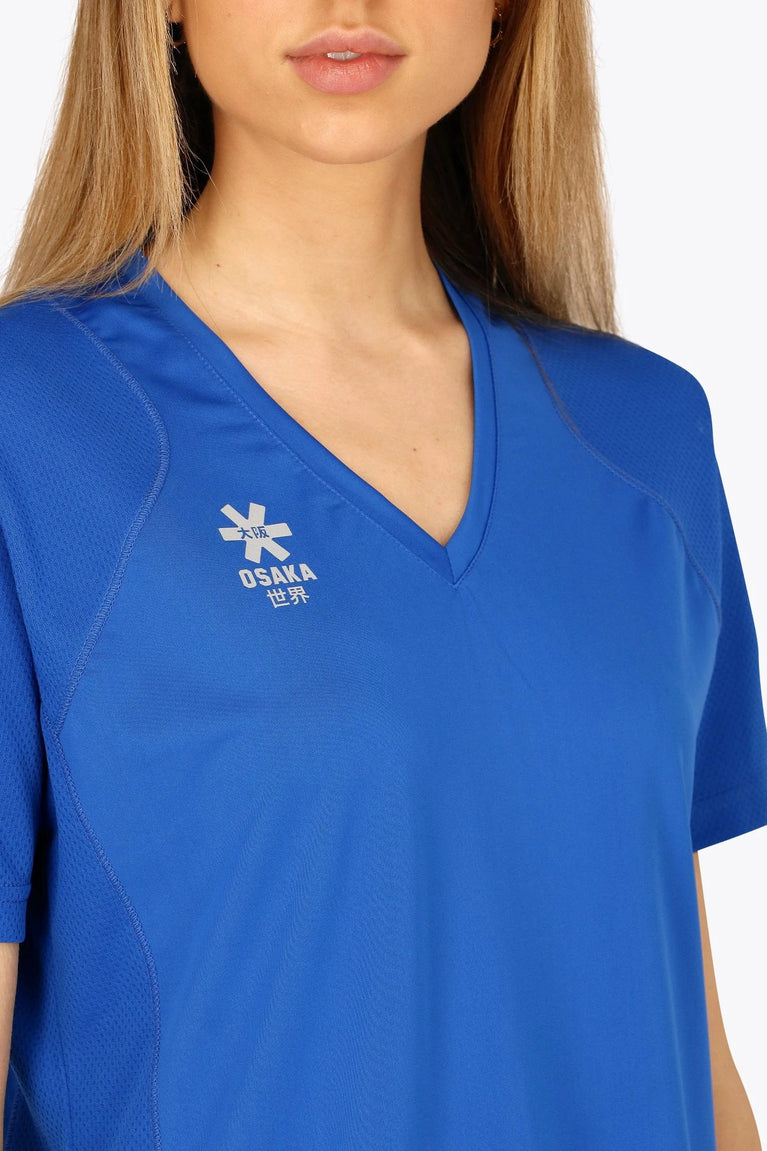 Woman wearing the Osaka women v-neck tech dress in princess blue with logo in grey. Front detail logo view