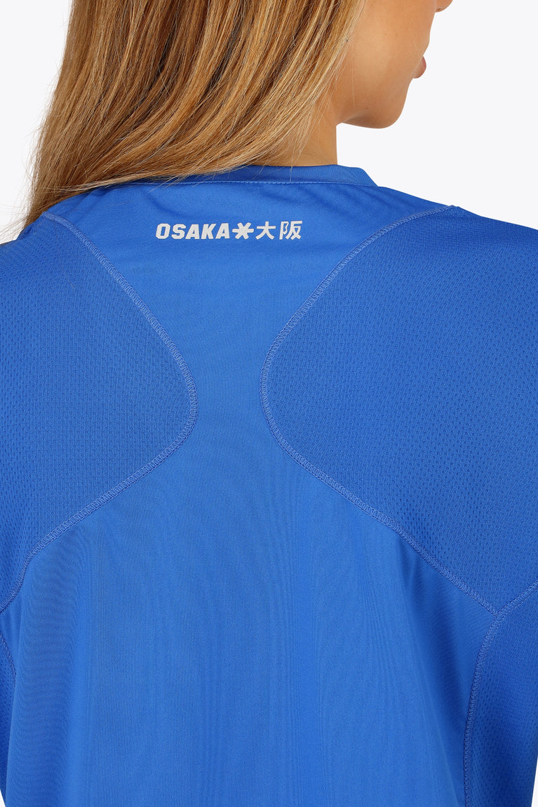 Woman wearing the Osaka women v-neck tech dress in princess blue with logo in grey. Back detail logo view