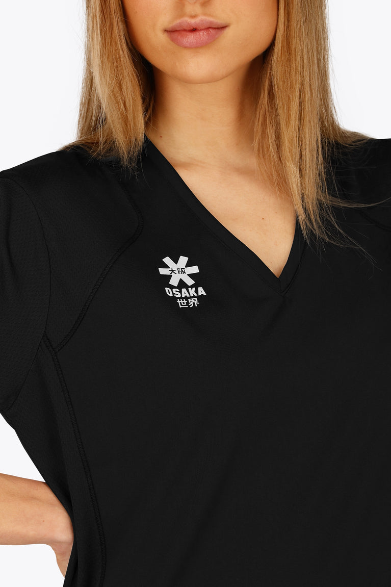 Woman wearing the Osaka women v-neck tech dress in black with logo in grey. Front detail logoview