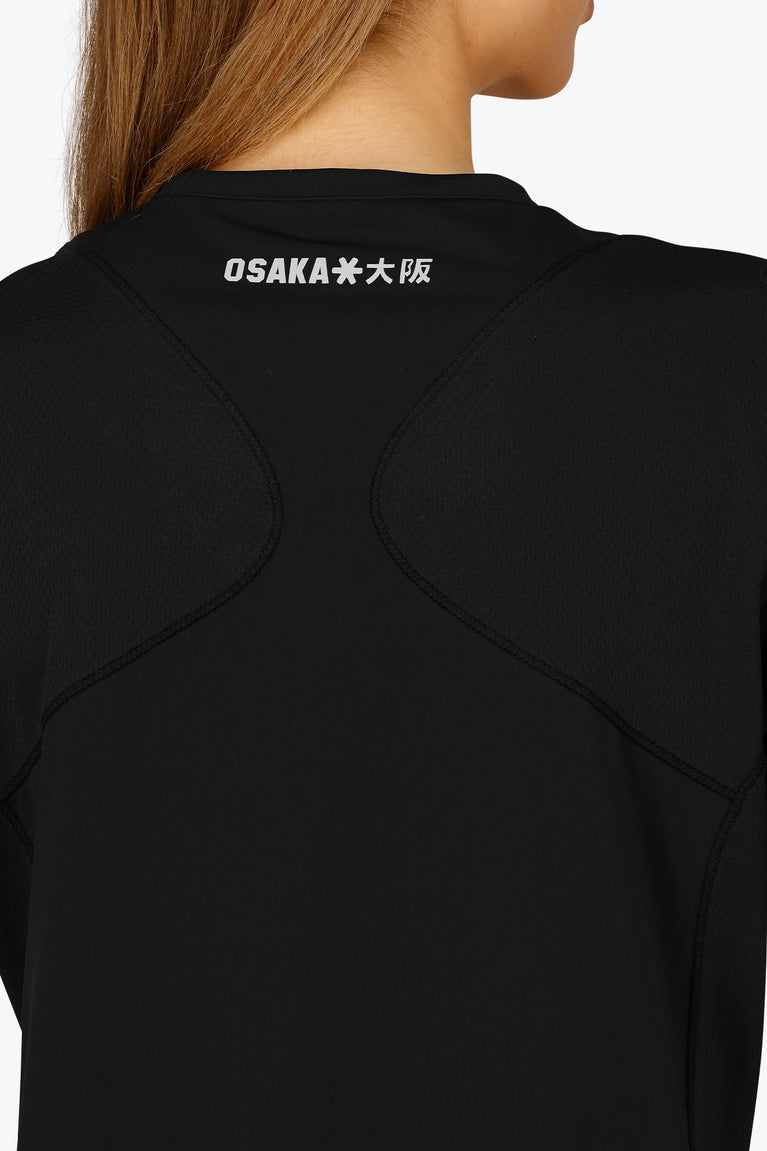 Woman wearing the Osaka women v-neck tech dress in black with logo in grey. Back detail logo view