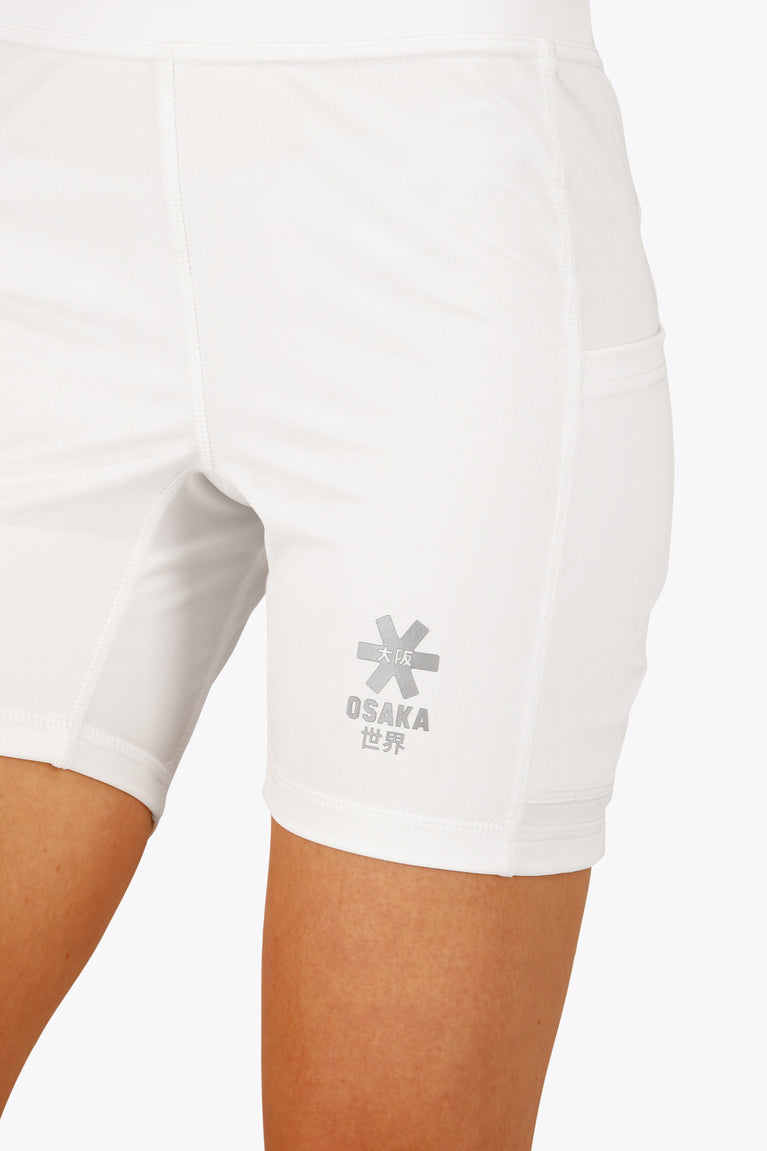 Woman wearing the Osaka women tech short thights in white with grey logo. Front detail logo view