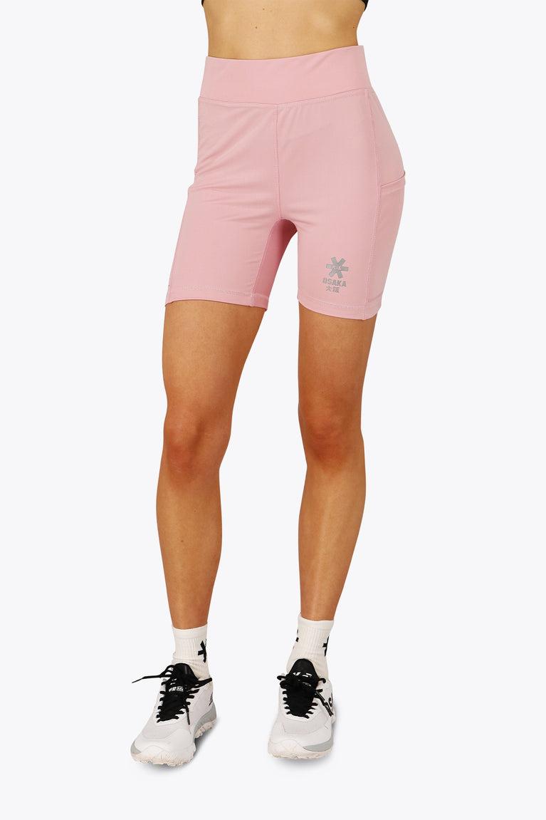 Woman wearing the Osaka women tech short thights in pink with grey logo. Front view