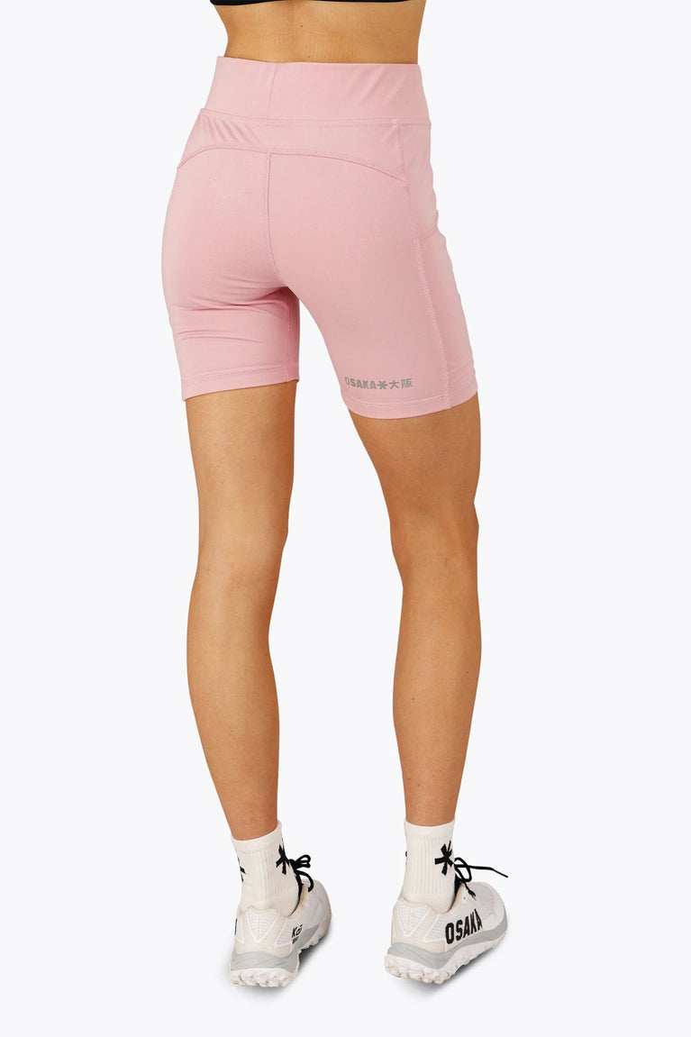 Woman wearing the Osaka women tech short thights in pink with grey logo. Back view