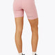 Woman wearing the Osaka women tech short thights in pink with grey logo. Back view