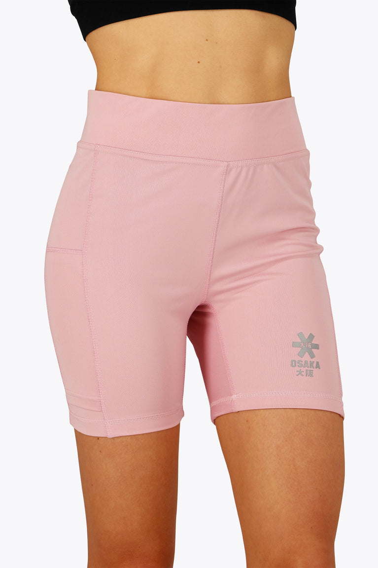 Woman wearing the Osaka women tech short thights in pink with grey logo. Front view
