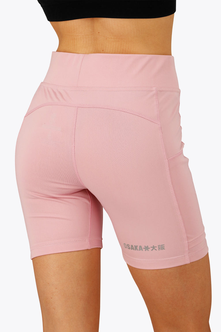 Woman wearing the Osaka women tech short thights in pink with grey logo. Back view