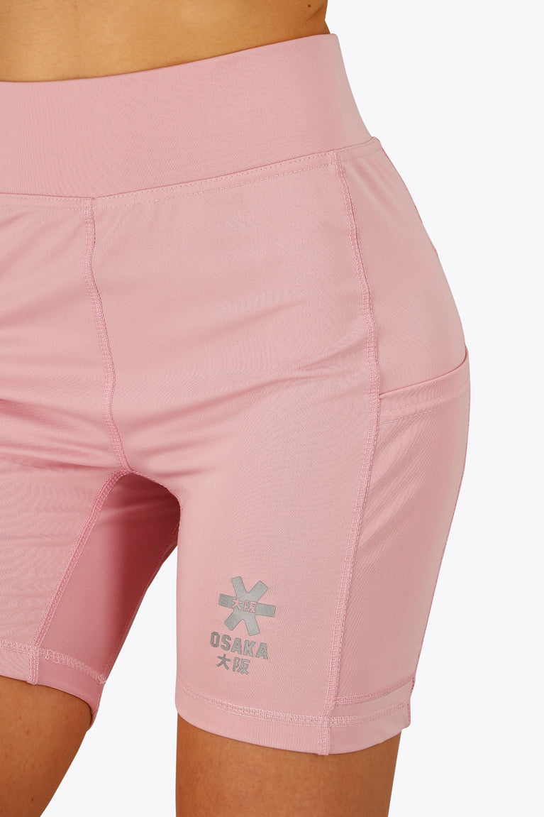Woman wearing the Osaka women tech short thights in pink with grey logo. Front view