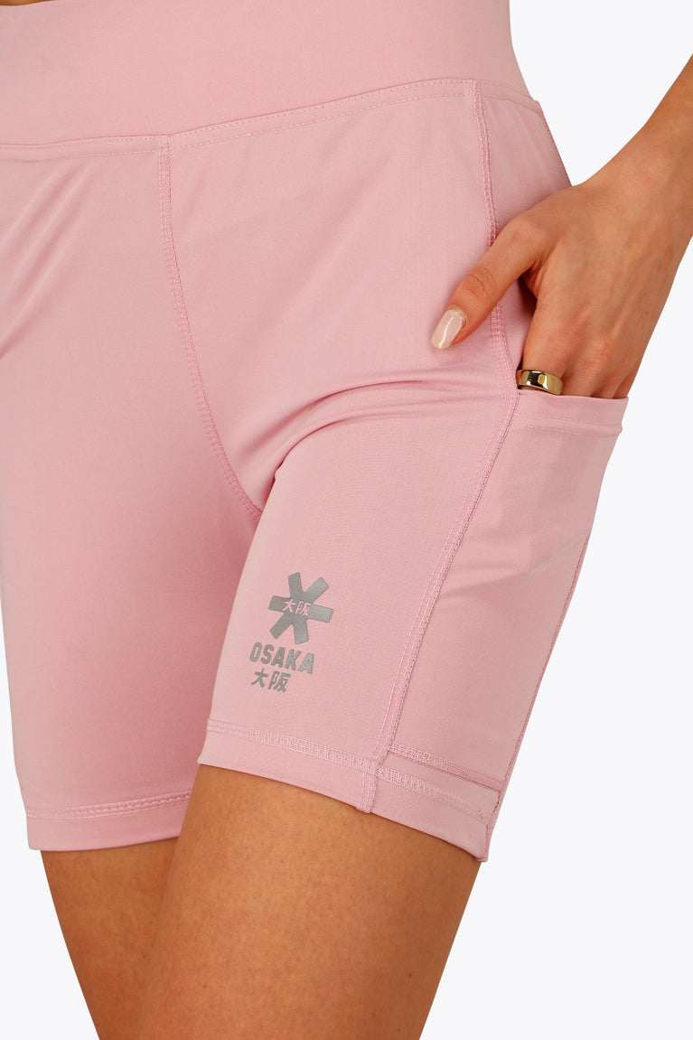 Woman wearing the Osaka women tech short thights in pink with grey logo. Front detail pocket view