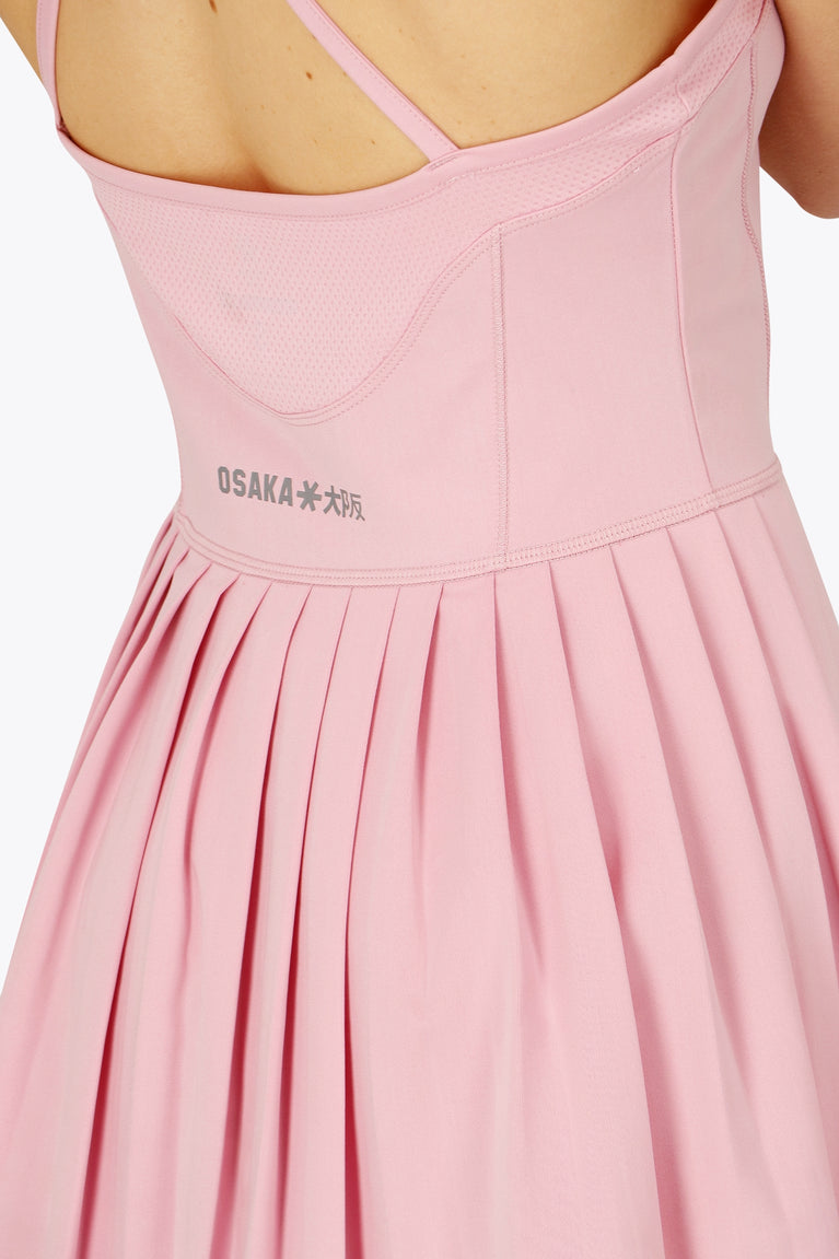 Woman wearing the Osaka women pleated tech dress in pink with grey logo. Back detail logo view