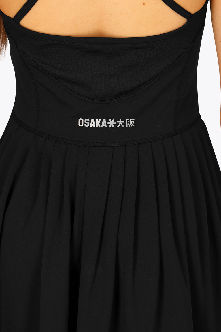 Woman wearing the Osaka women pleated tech dress in black with grey logo. Back detail logo view