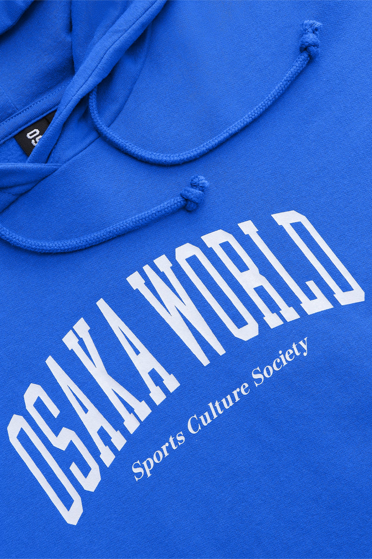 Osaka women cropped hoodie inprincess blue with college logo in white. Front flatlay detail logo view