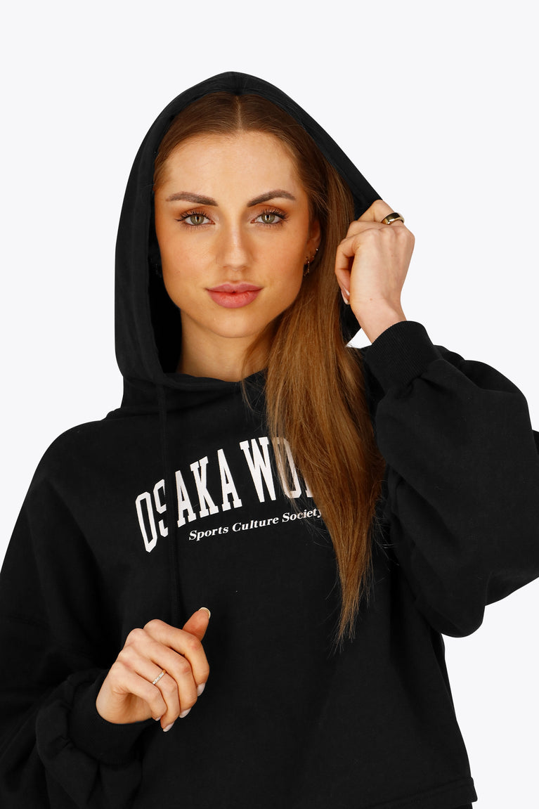 Woman wearing the Osaka women cropped hoodie in black with college logo in white. Front view