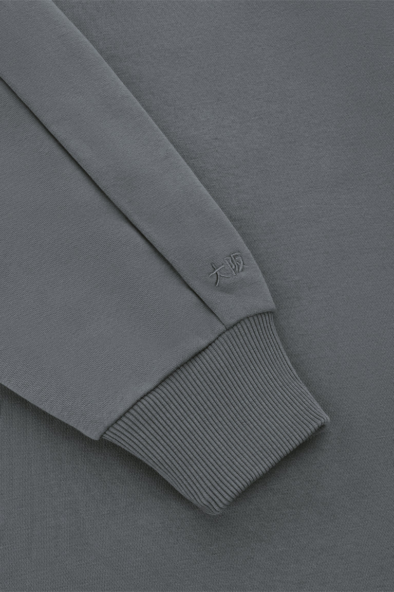 Dark grey half-zip sweater sleeve cuff with small logo stitch and ribbed trim