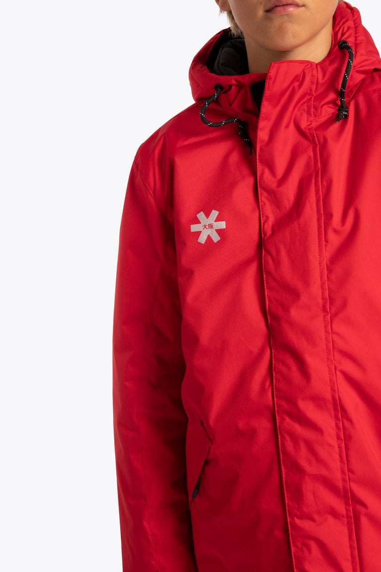 Boy wearing the Osaka Kids Stadium Jacket in Red. Front detail logo view