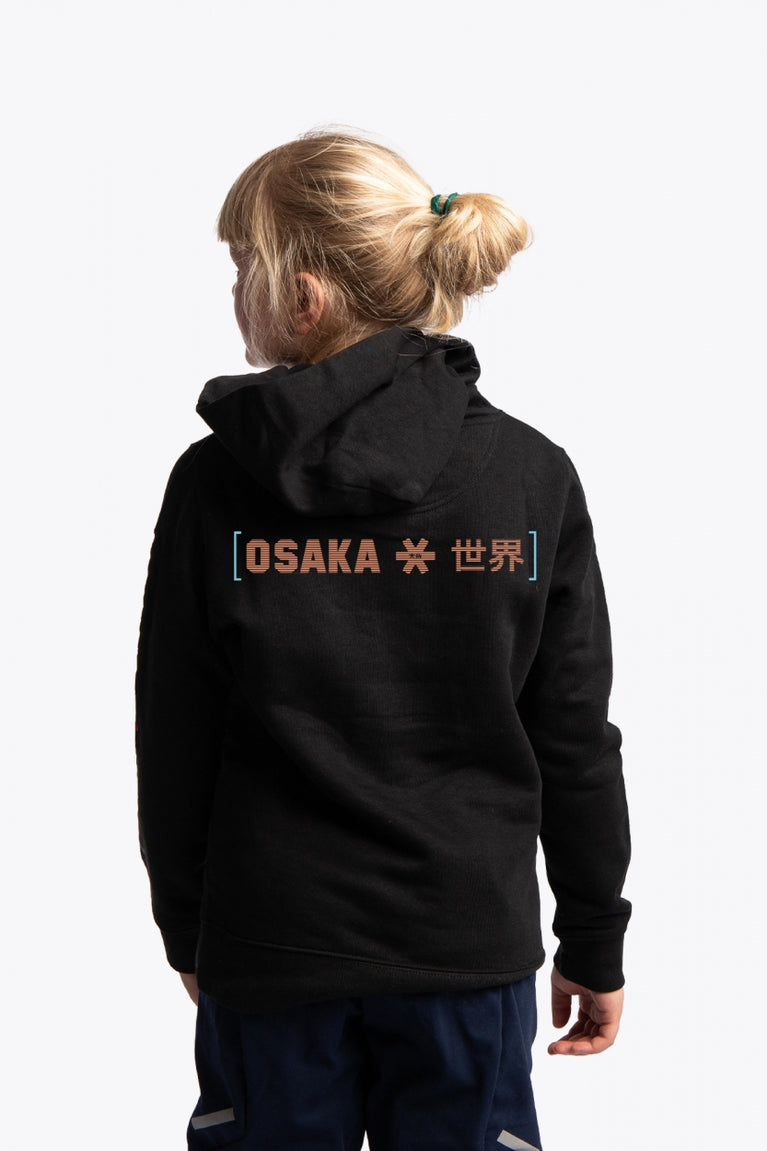 Girl wearing the Osaka kids trace hoodie in black with logo in orange and blue. Back view