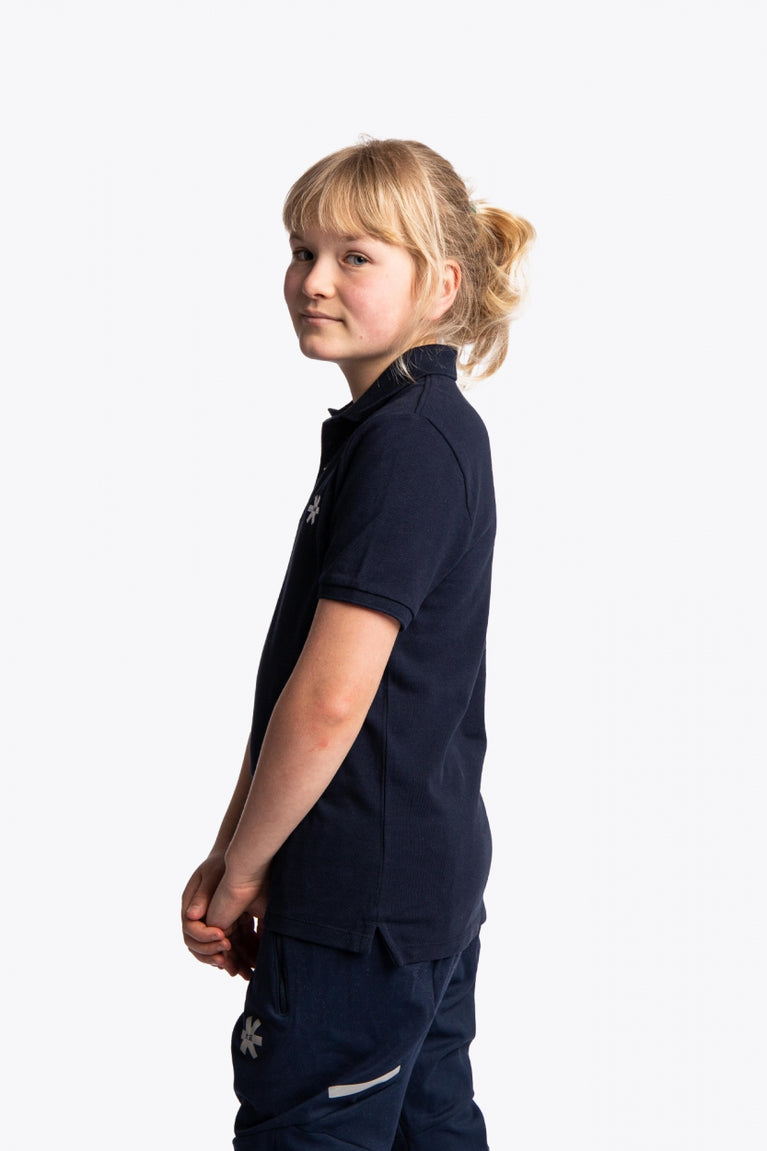 Girl wearing the Osaka kids polo in navy with logo in white. Side view