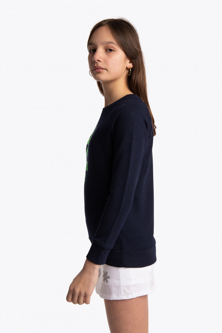 Girl wearing the Osaka kids sweater in navy with logo in green. Side view