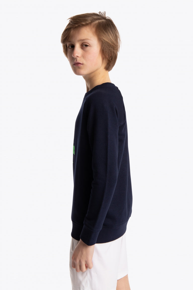 Boy wearing the Osaka kids sweater in navy with logo in green. Side view