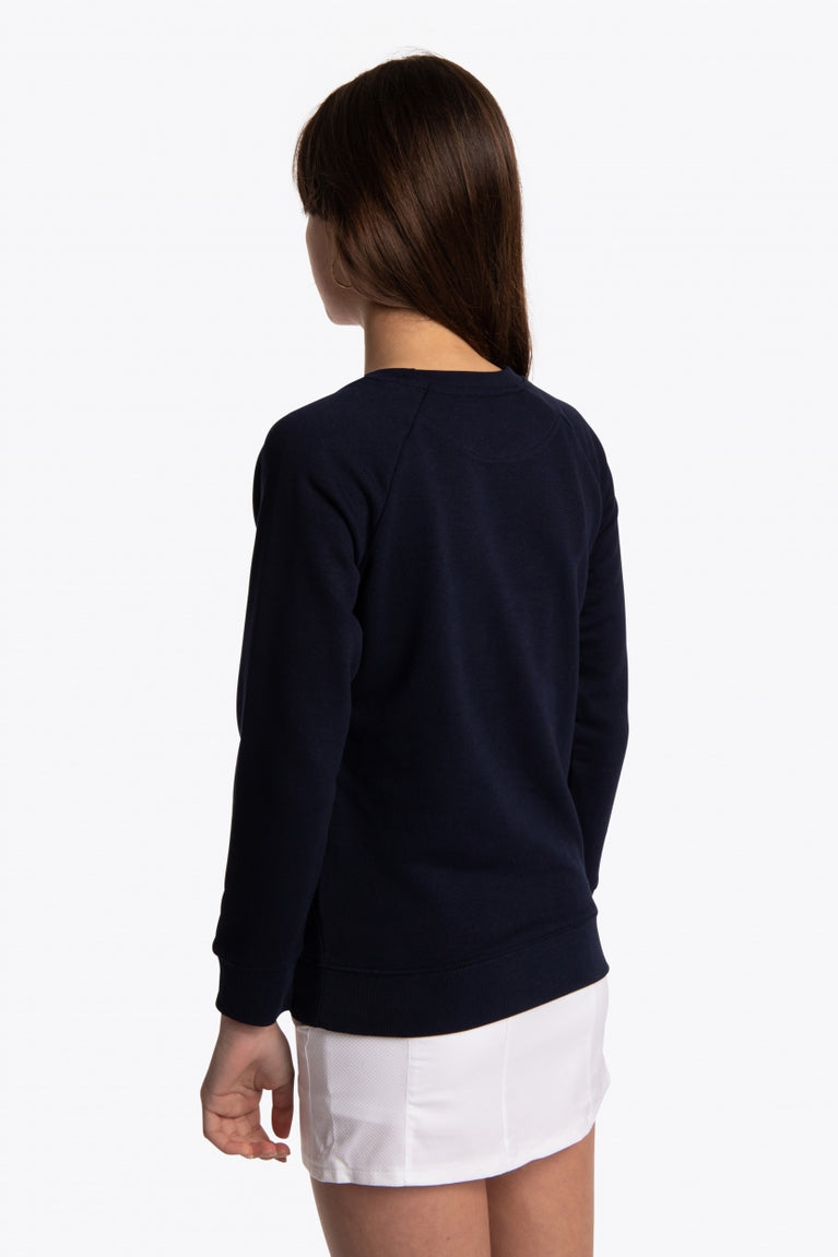 Girl wearing the Osaka kids sweater in navy with pink logo. Side/back view