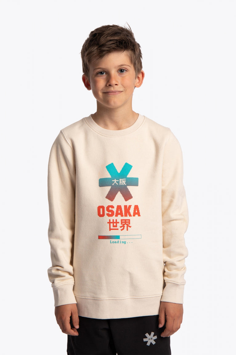 Boy wearing the Osaka kids pixo sweater in natural raw with orange and blue logo. Front view