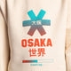 Osaka kids pixo sweater in natural raw with orange and blue logo. Detail view logo