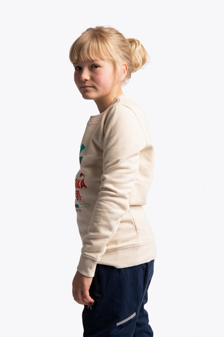 Girl wearing the Osaka kids pixo sweater in natural raw with orange and blue logo. Side view
