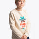 Girl wearing the Osaka kids pixo sweater in natural raw with orange and blue logo. Front view