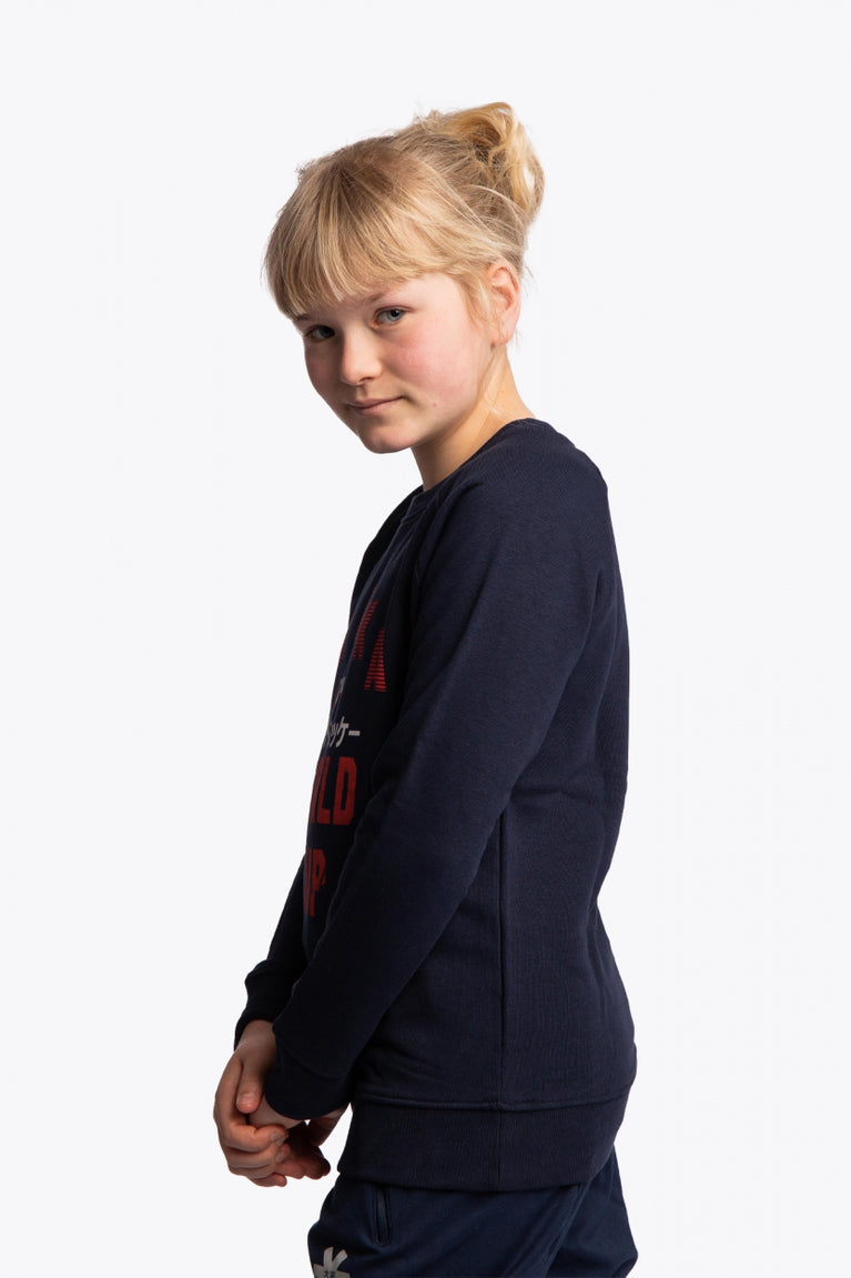 Girl wearing the Osaka kids worldcup sweater in navy with orange logo. Side view