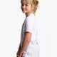 Girl wearing the Osaka kids service games tee short sleeve white with logo in blue. Side view