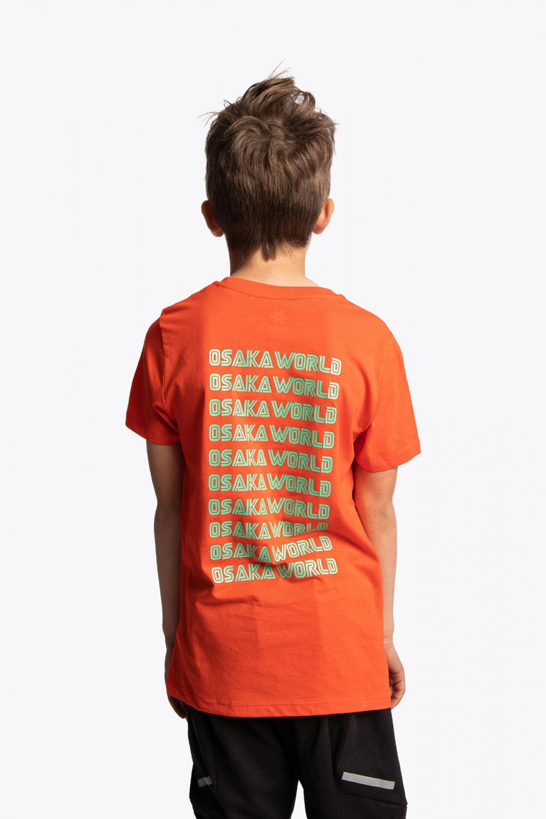 Boy wearing the Osaka kids service games tee short sleeve orange with logo in green. Back view