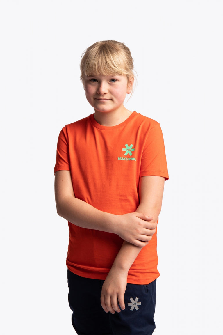 Girl wearing the Osaka kids service games tee short sleeve orange with logo in green. Front view