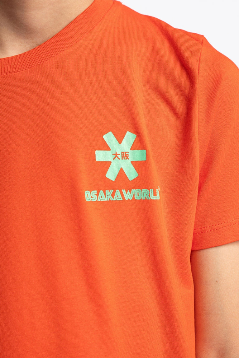 Osaka kids service games tee short sleeve orange with logo in green. Detail view logo front