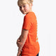 Girl wearing the Osaka kids service games tee short sleeve orange with logo in green. Side view