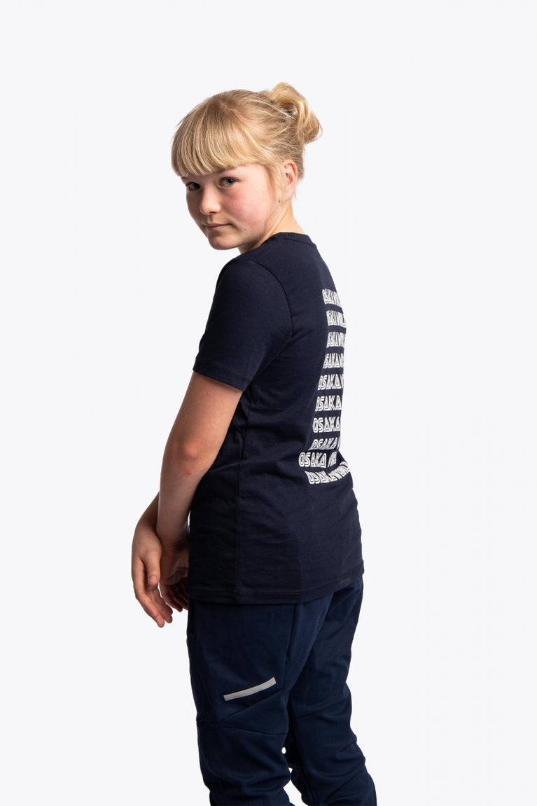 Girl wearing the Osaka kids service games tee short sleeve navy with logo in white. Back/side view