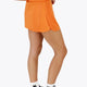 Woman wearing the Osaka women ball skort in orange with logo in white. Side view