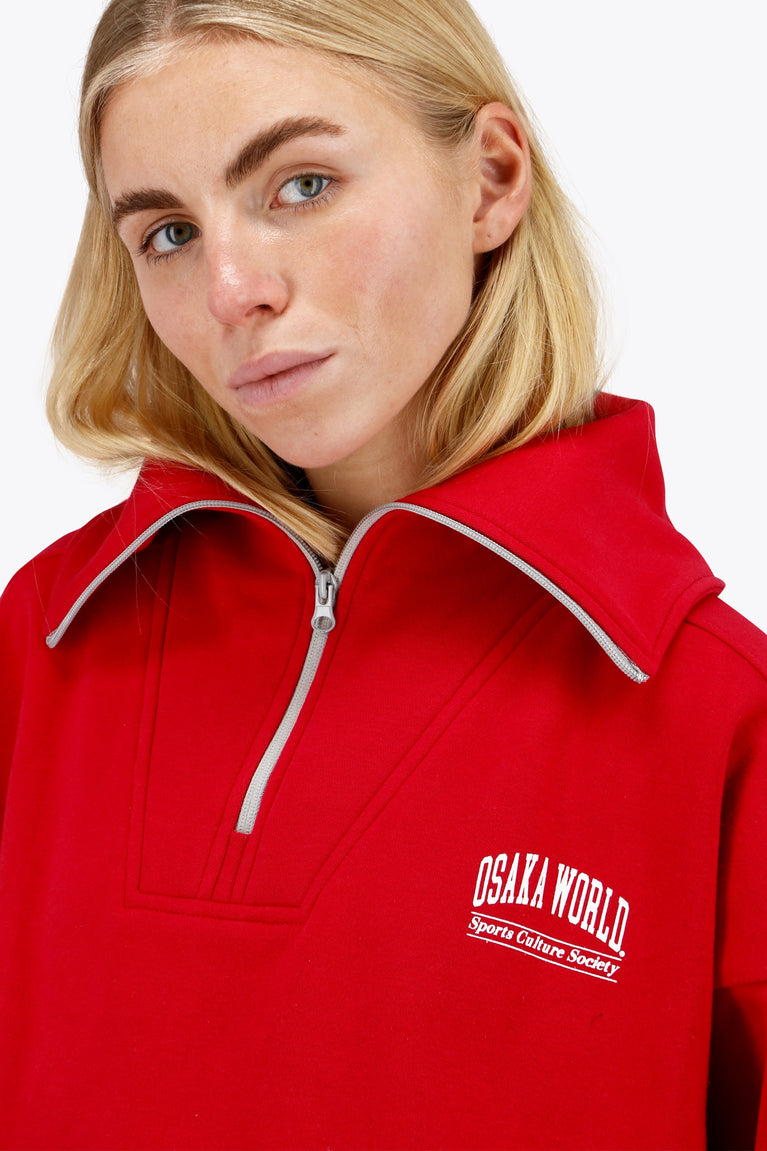 Woman wearing the Osaka women half zip sweater in red with white logo. Front detail neck view