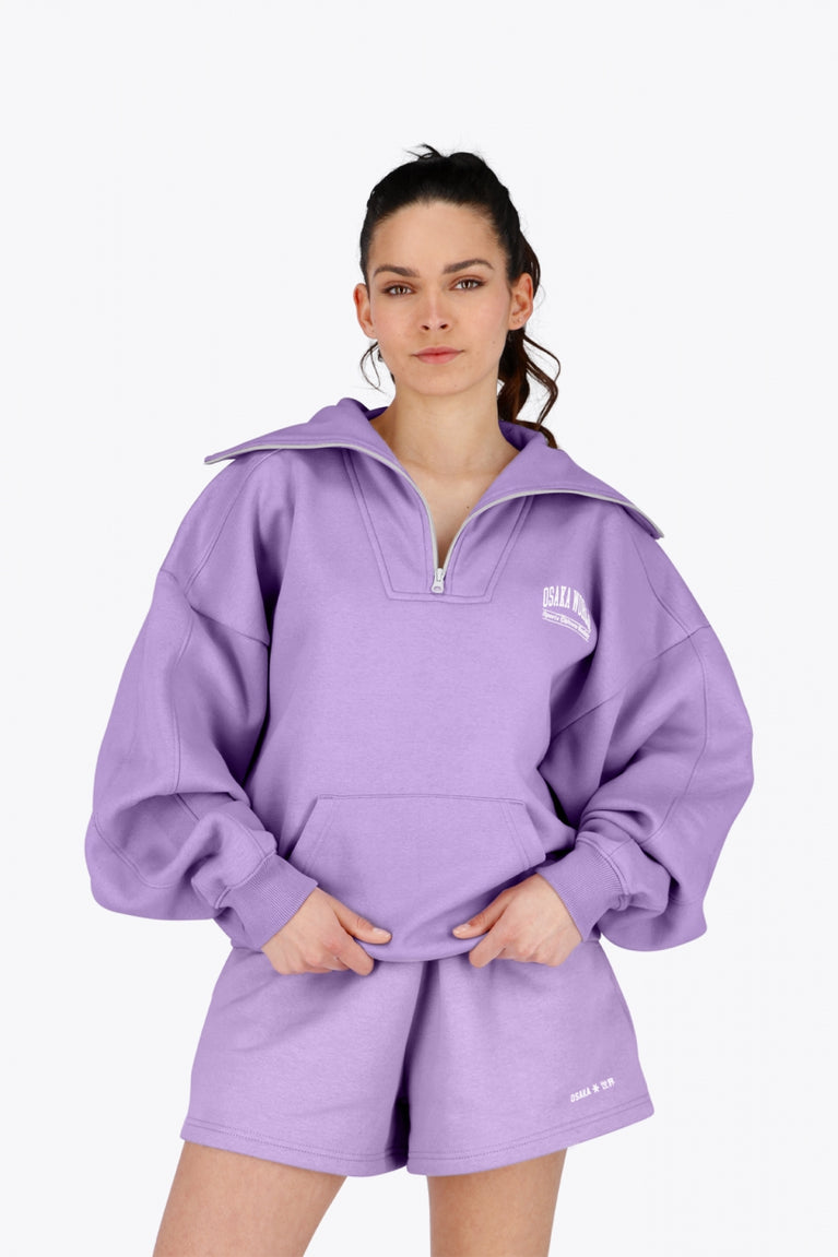 Woman wearing the Osaka women half zip sweater in light purple with white logo. Front view