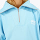 Woman wearing the Osaka women half zip sweater in light blue with white logo. Front detail neck view