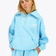 Woman wearing the Osaka women half zip sweater in light blue with white logo. Front view