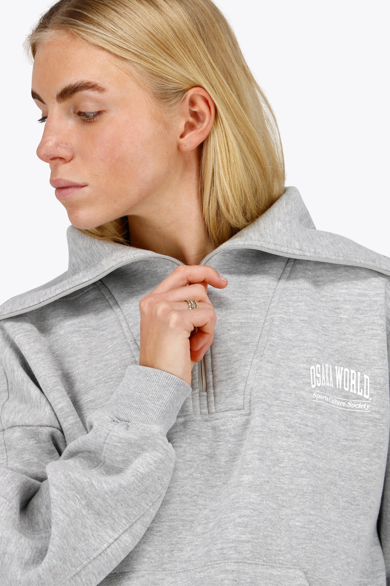 Woman wearing the Osaka women half zip sweater in heather grey with white logo. Front detail neck view