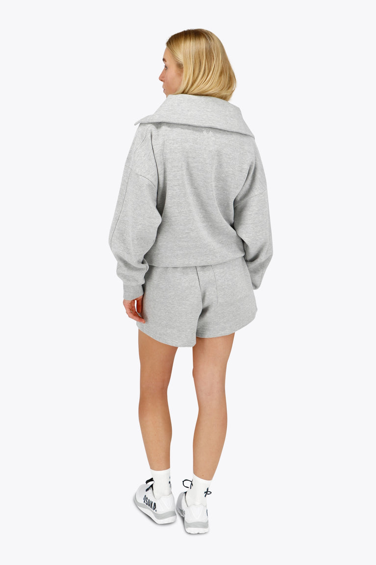 Woman wearing the Osaka women half zip sweater in heather grey with white logo. Back view